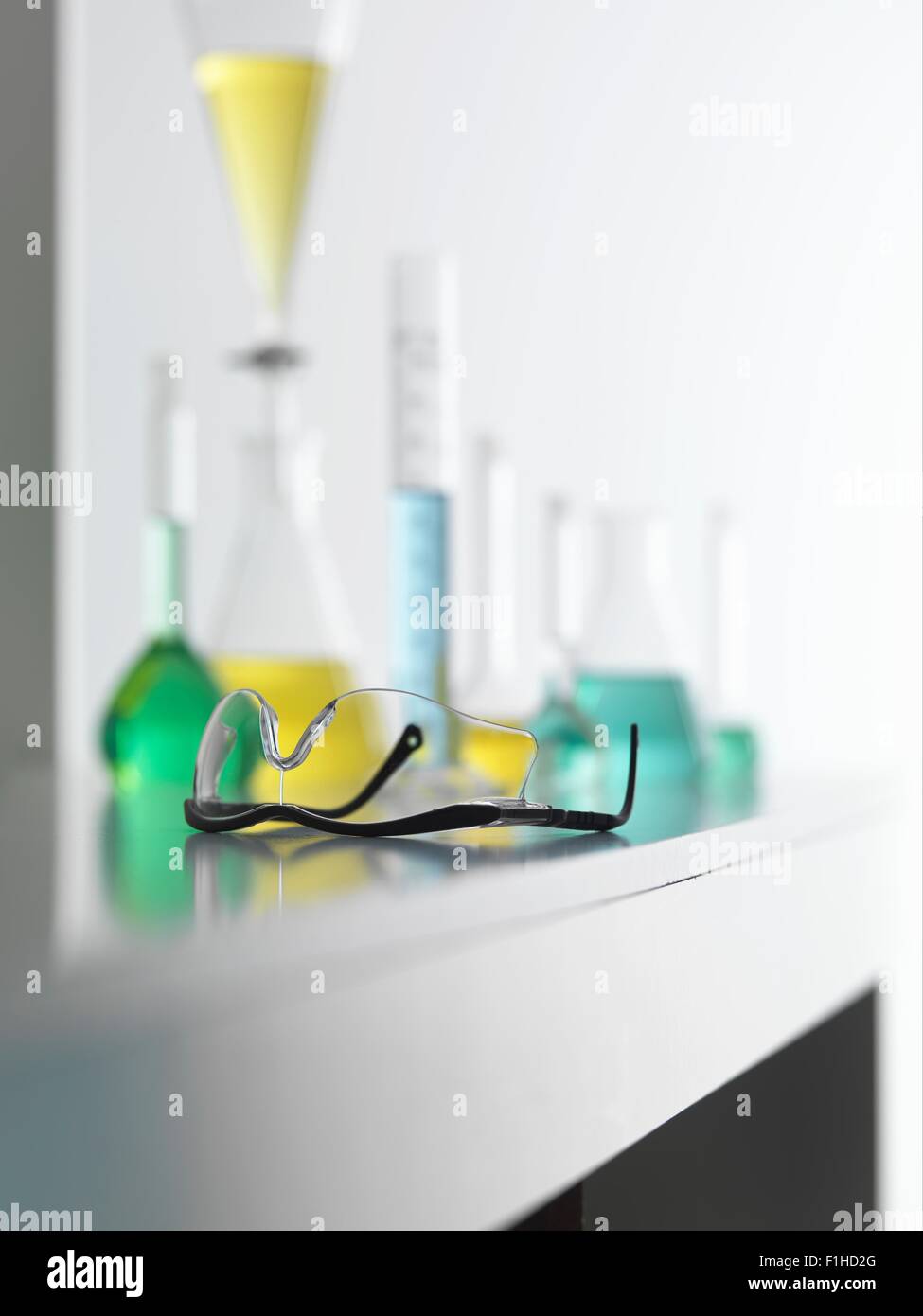 Laboratory safety glasses on lab bench with a chemical experiment in background Stock Photo