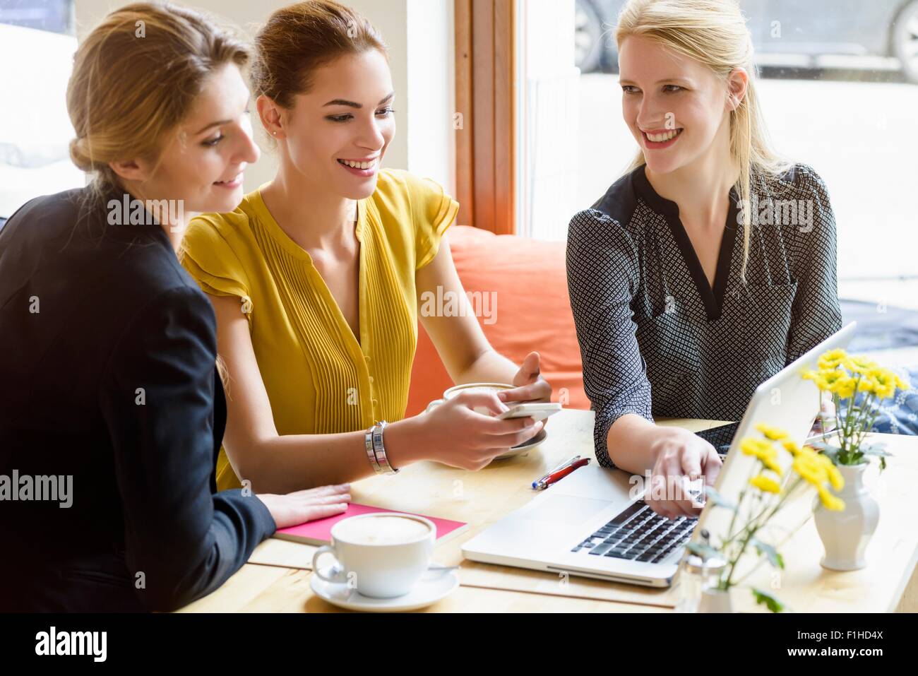 Three young women looking at laptop in cafe Stock Photo