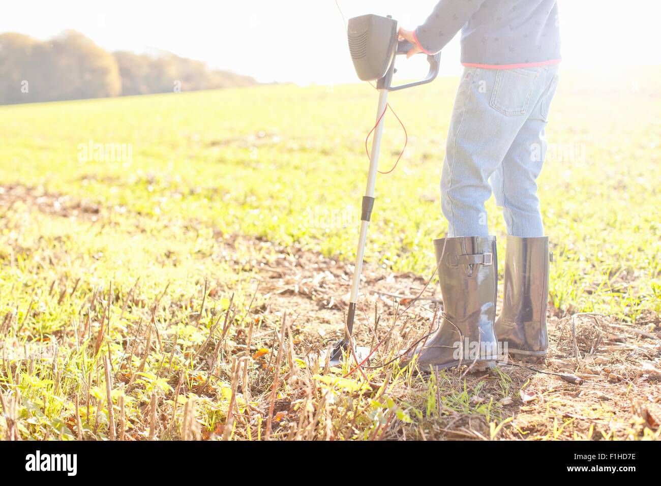 Waist down view of girl using metal detector in field Stock Photo