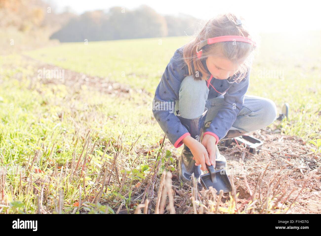 Girl with metal detector crouching and digging with spade in field Stock Photo