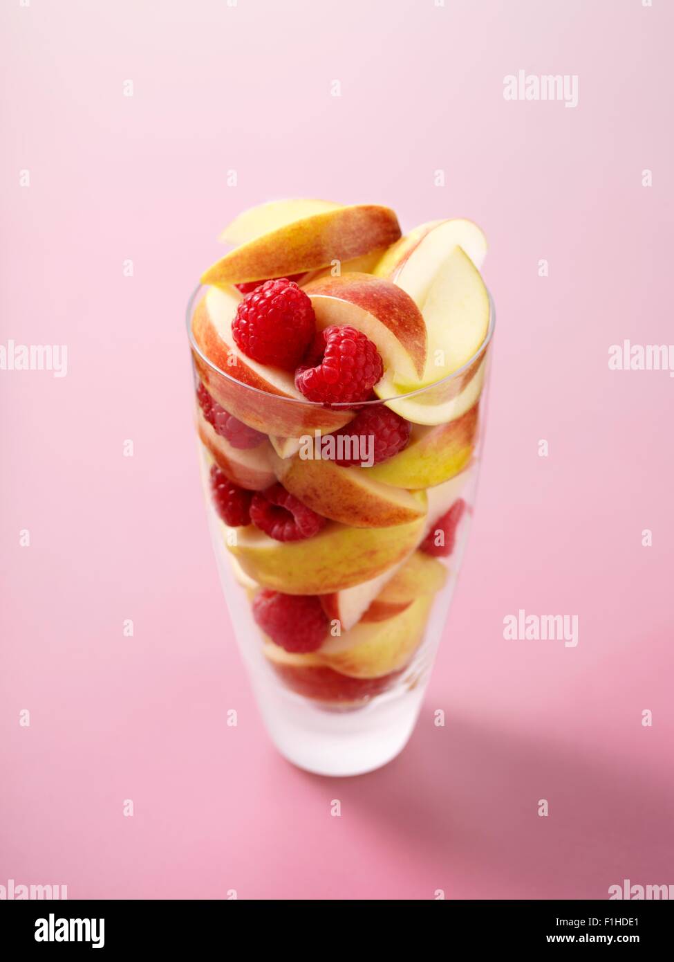 Glass full of raspberries and apple slices on pink background Stock Photo