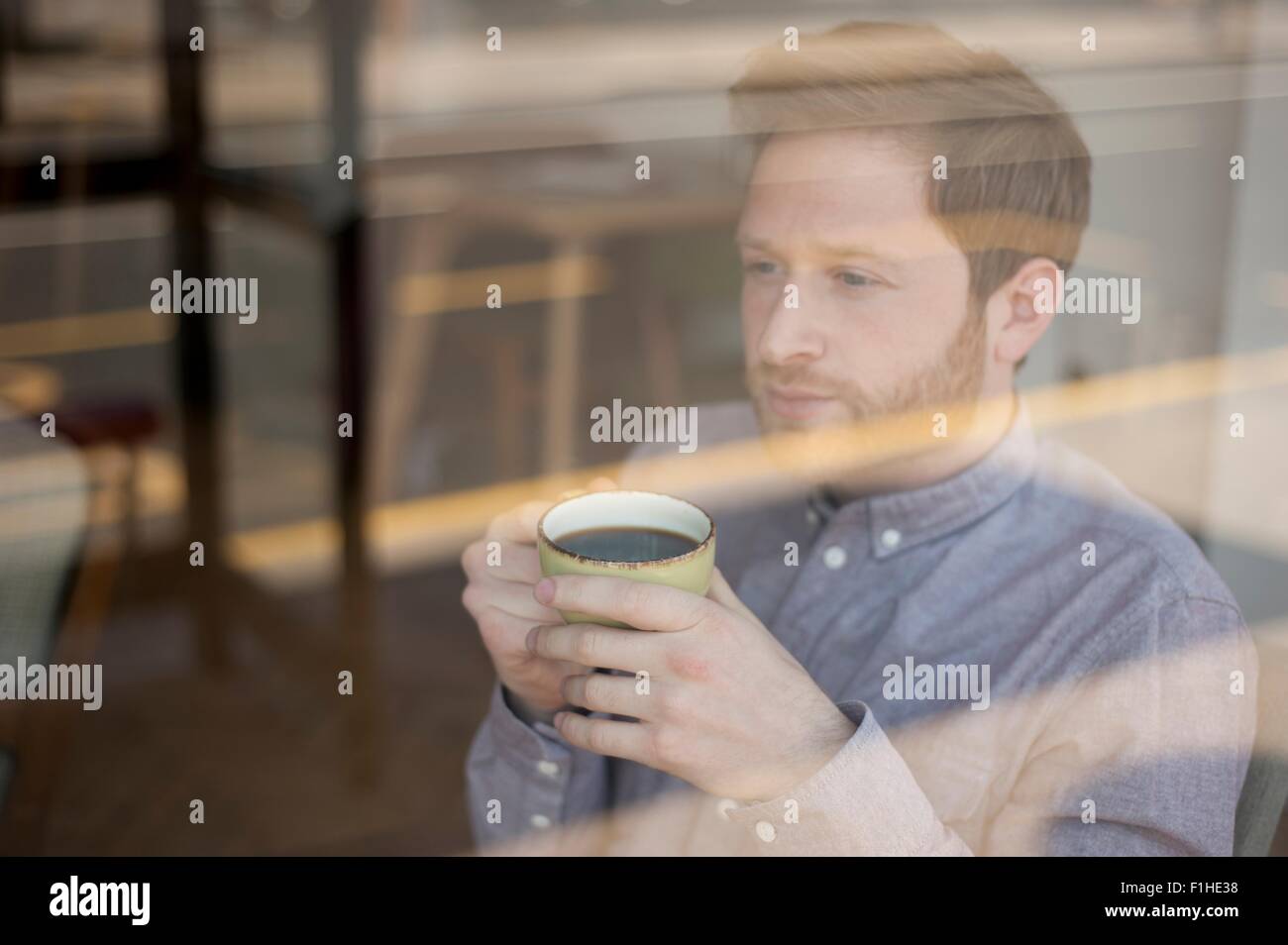 Male customer behind cafe window drinking coffee and gazing Stock Photo