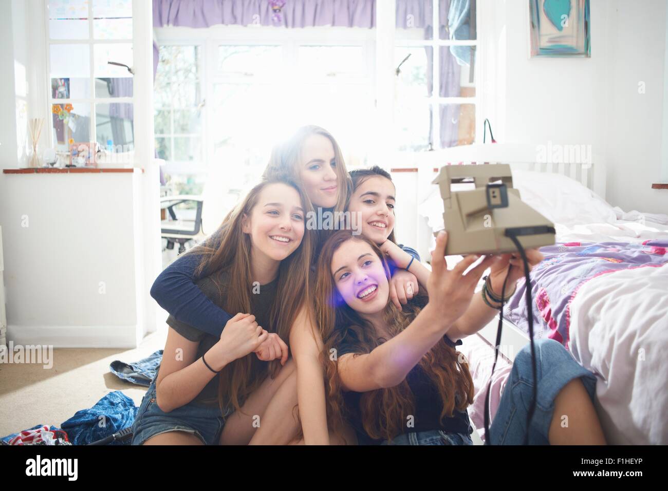 Four teenage girls taking instant camera selfie in bedroom Stock Photo