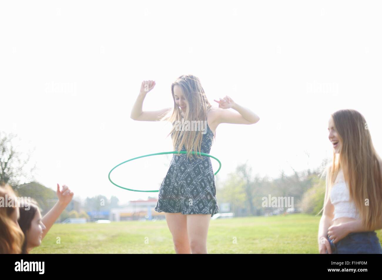 Teenage girl hoola hooping for friends in park Stock Photo