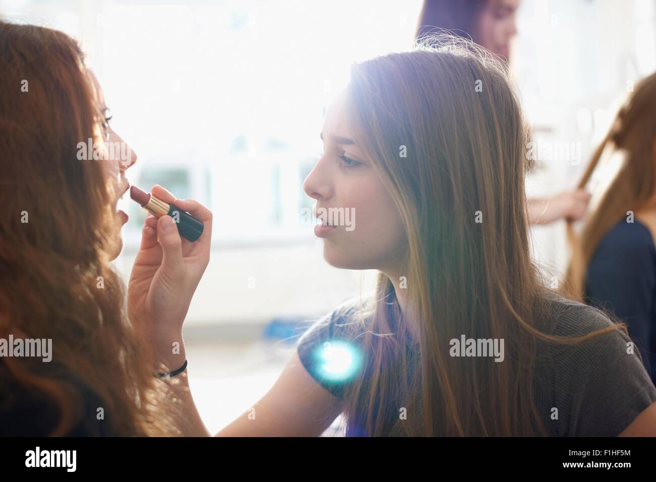 Teenage girl having lipstick applied by best friend in bedroom Stock Photo