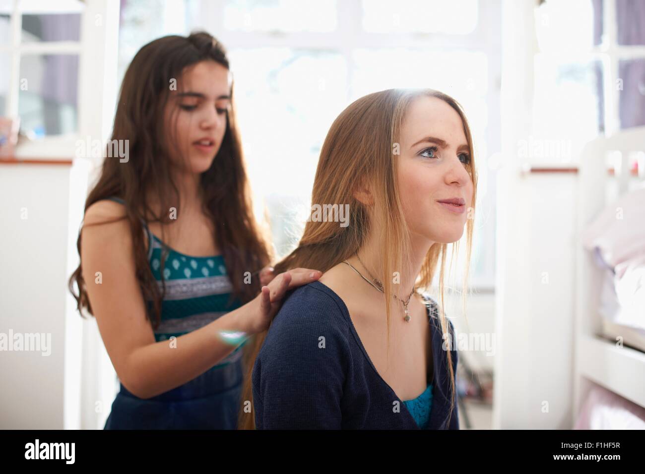 Teenage girl having hair plated by best friend in bedroom Stock Photo