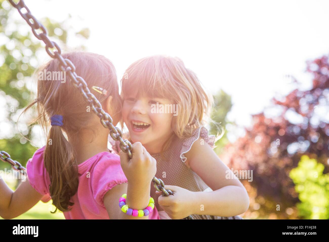 Two young girls swinging face to face on park swing Stock Photo