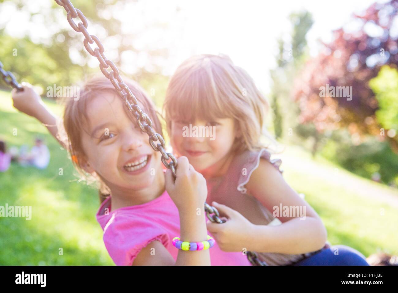 Portrait of two young girls swinging together on park swing Stock Photo