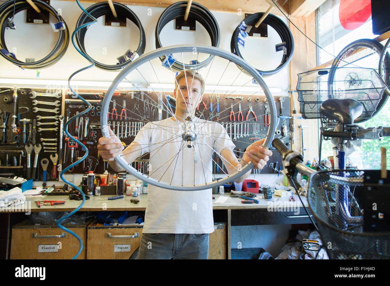 Mid adult man in repair shop looking through bicycle wheel Stock Photo