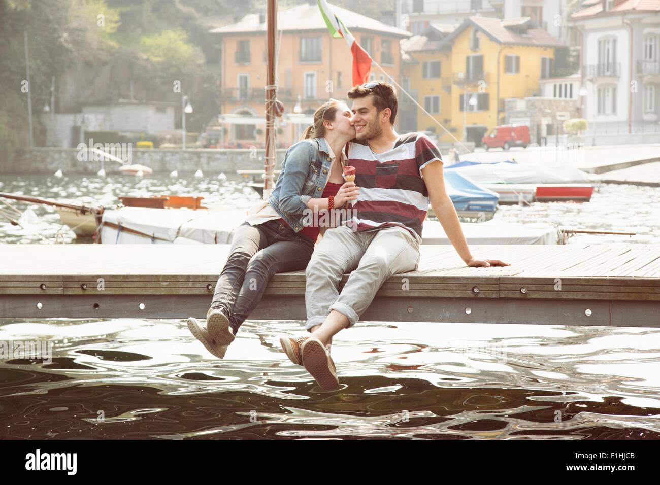 Couple sitting on pier whispering and eating ice cream cone at lake Mergozzo, Verbania, Piemonte, Italy Stock Photo