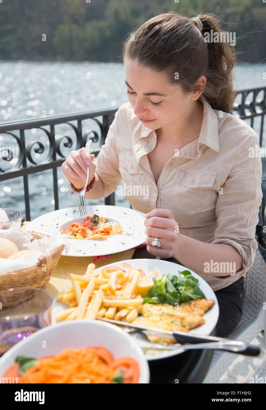 Young woman eating lunch at lakeside restaurant, Lake Mergozzo, Verbania, Piemonte, Italy Stock Photo