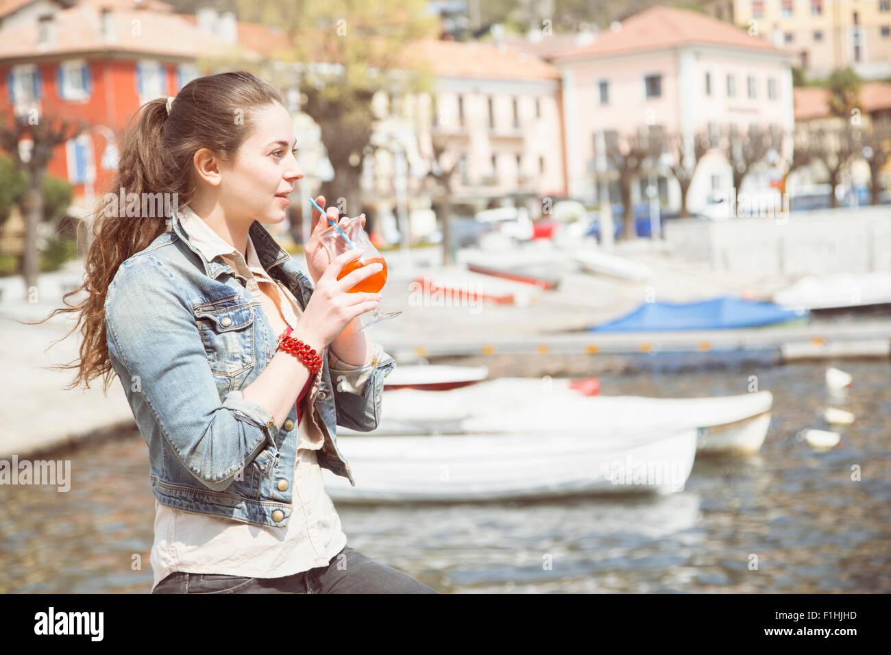 Young woman drinking cocktail on lakeside, Lake Mergozzo, Verbania, Piemonte, Italy Stock Photo
