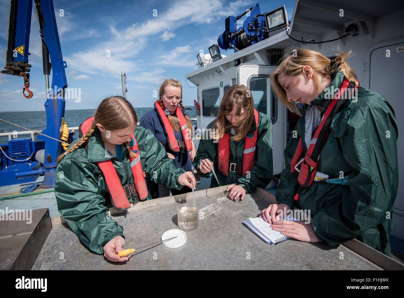 Student marine biologists test sea water sample on research ship Stock