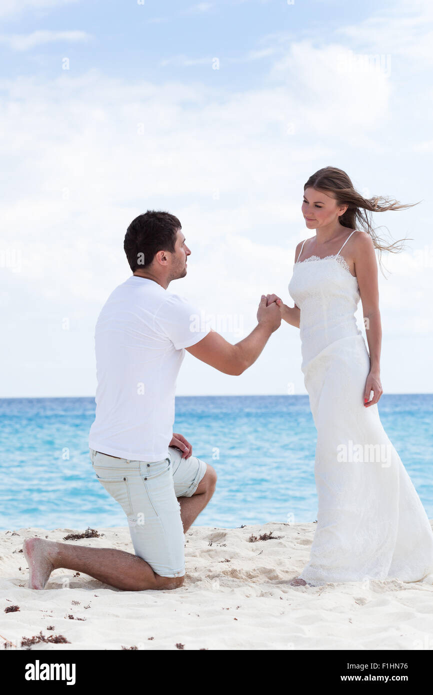 Man down on one knee and asking for marry his woman, holding her hand on sandy beach near sea at Caribbean vacation. Stock Photo