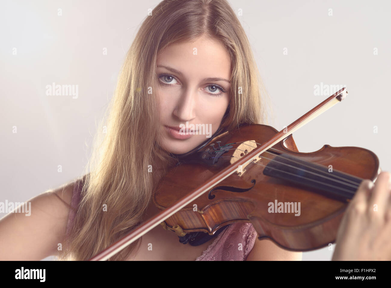 Pretty young female violinist in a stylish pink outfit standing playing the violin as she gives a classical recital at the acade Stock Photo