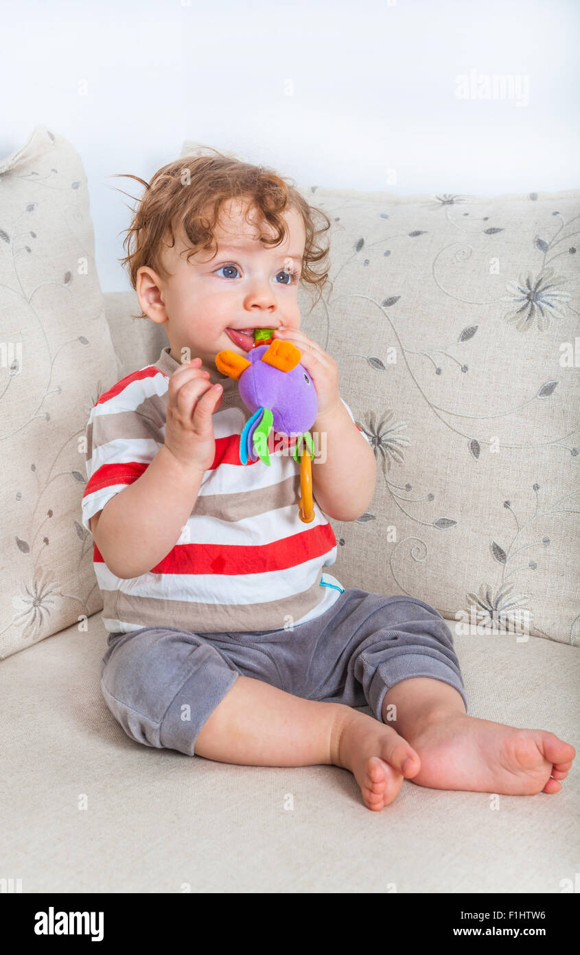 11 months old baby boy chewing on a toy on the sofa at home. Stock Photo