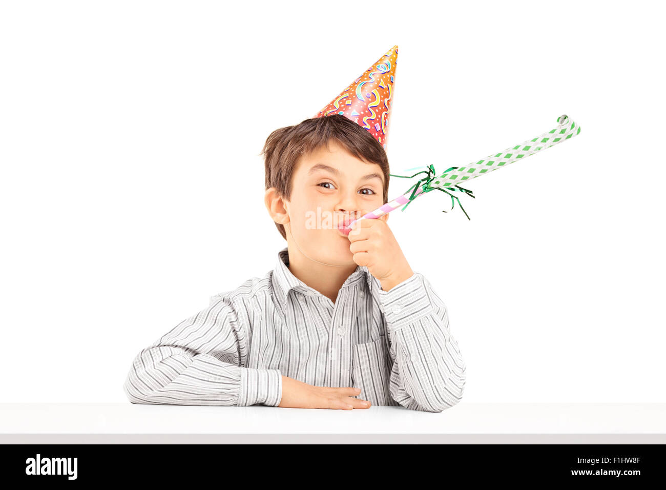 Little kid with party hat sitting at a table and blowing a favor horn isolated on white background Stock Photo