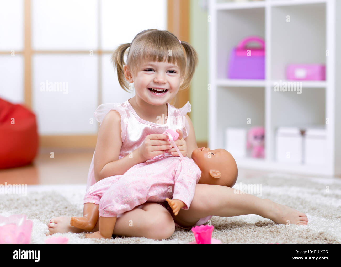 Kid girl plays with doll at home in the children room Stock Photo