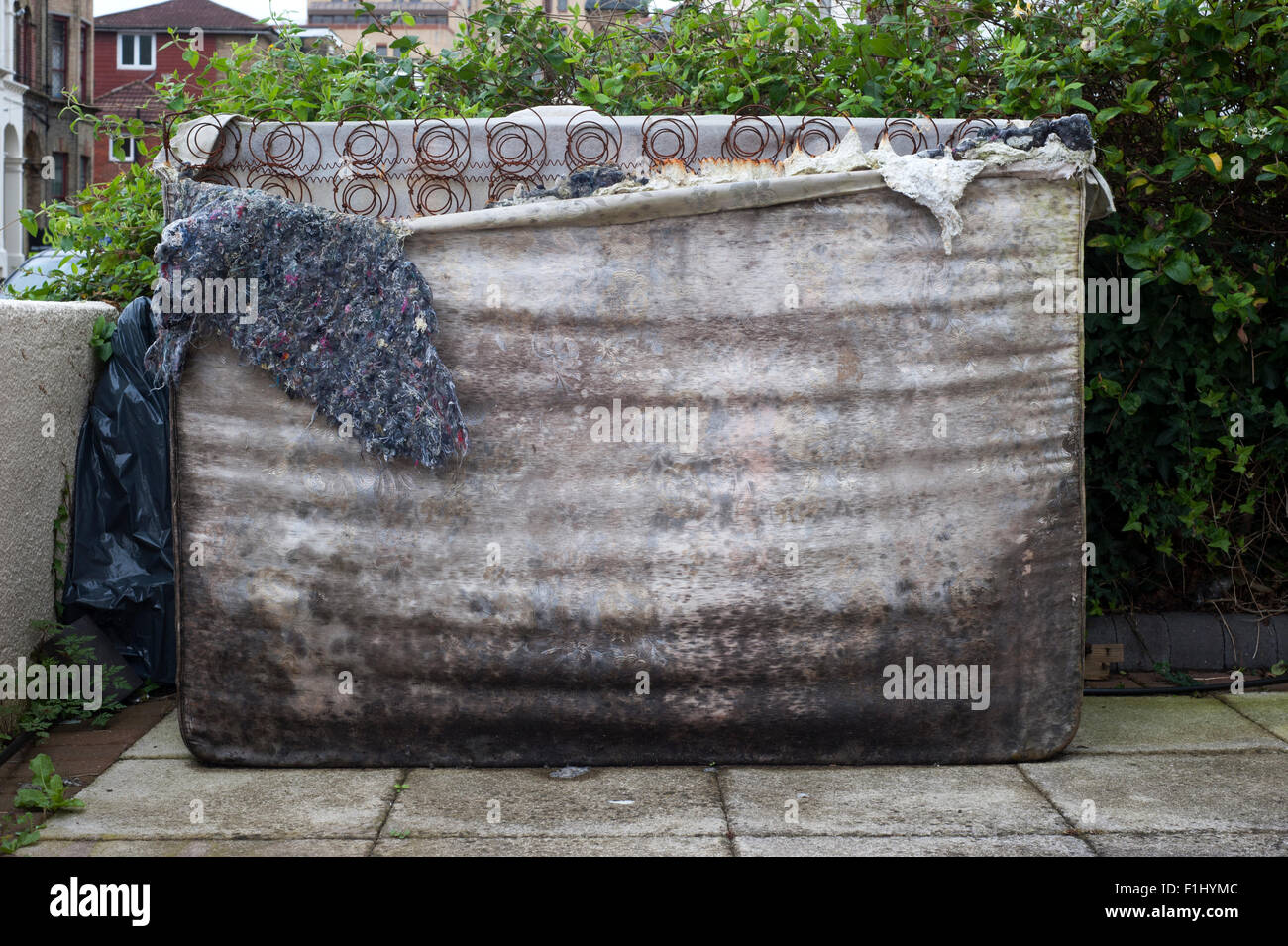 torn and mouldy mattress dumped in a front garden awaiting disposal