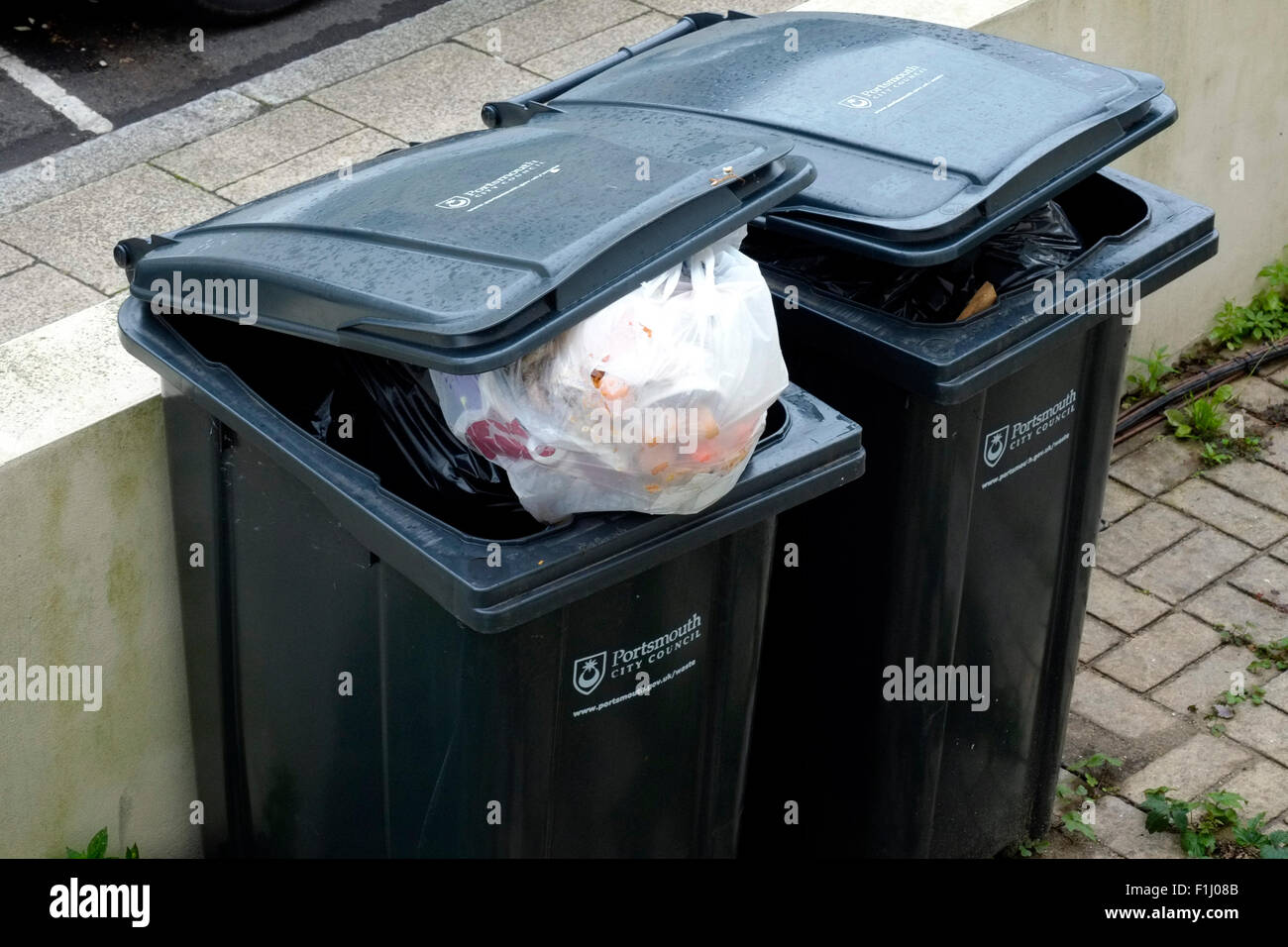 overflowing wheelie bins with the lids ajar awaiting refuse collection england uk Stock Photo