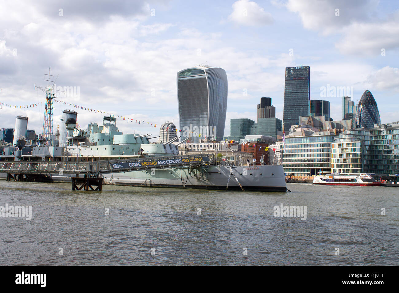 HMS Belfast, famous warship on River Thames. London City on a background. Tourists walking on the deck of the ship. Stock Photo