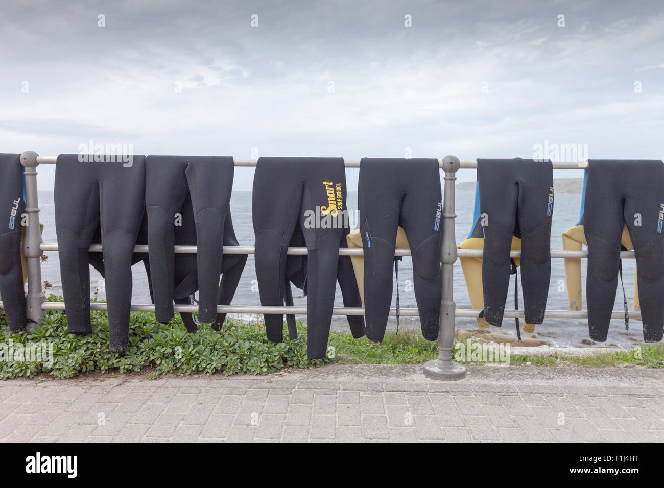 Eight wetsuits draped over a rail on the roadside in Sennen Cove, Cornwall, a noted surfing and watersports area. UK Stock Photo