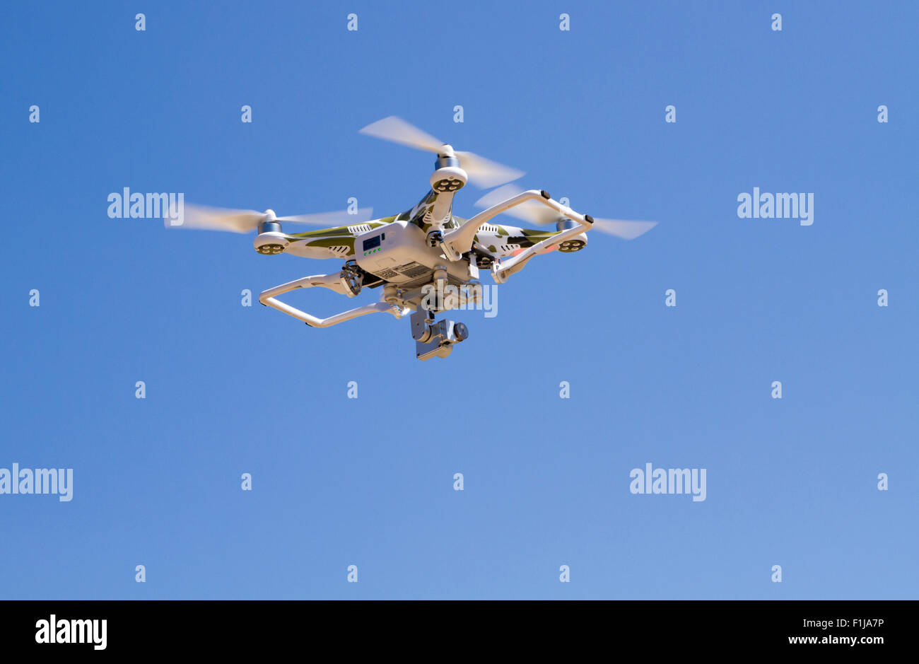Camouflage Quadrocopter hovering  against a blue sky with landing gear up Stock Photo
