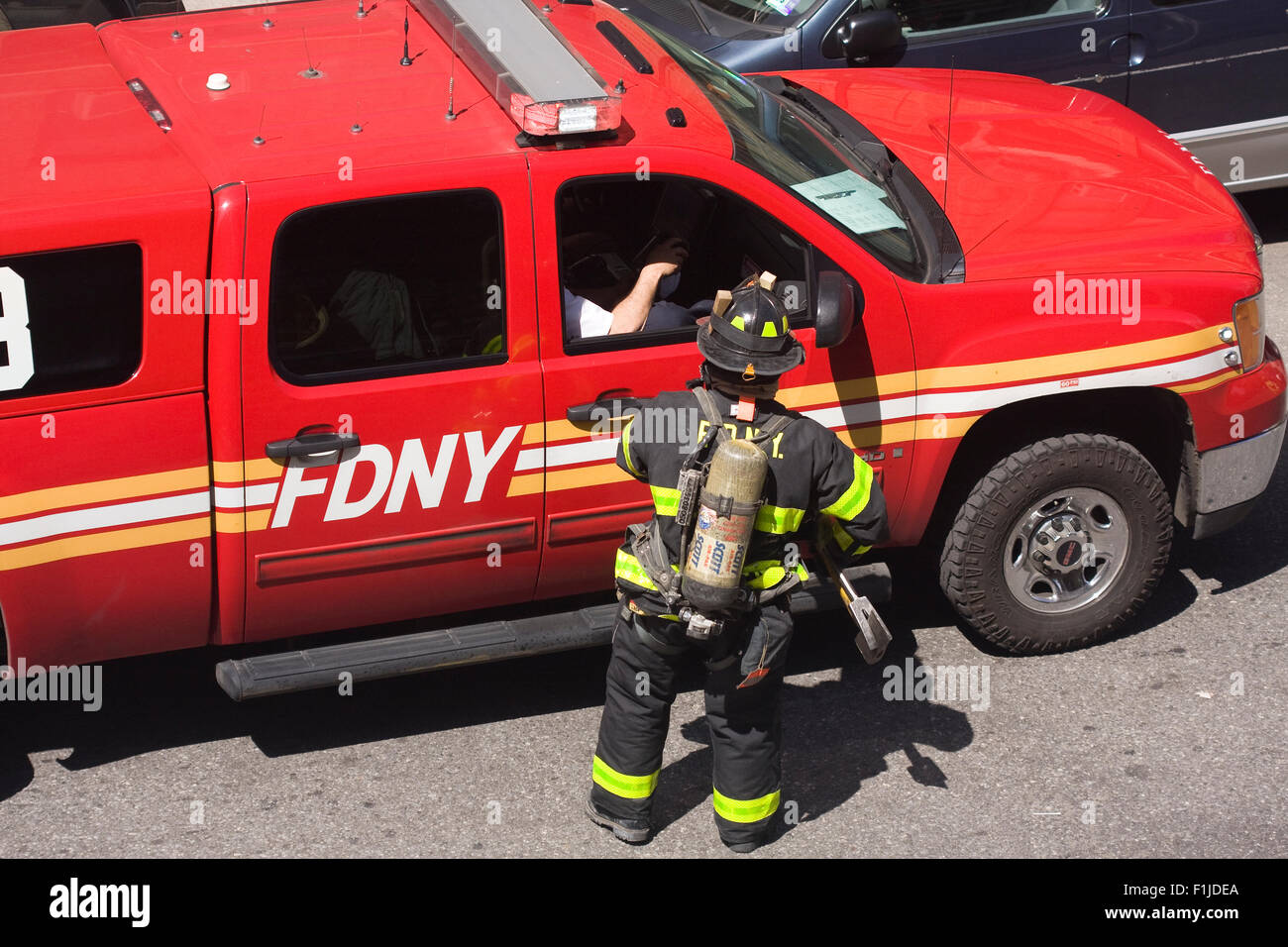 FDNY Firefighter in full turnout gear speaks with his supervisor in a red pickup truck on the street. Stock Photo