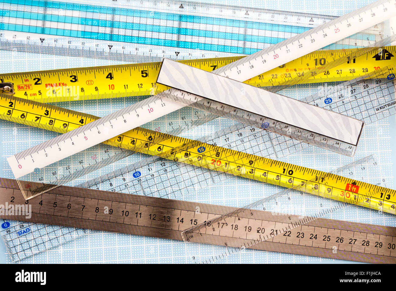 Overhead view of several different rulers and metal tape measures. Yellow tape measure, with white, grey and other rulers. Stock Photo