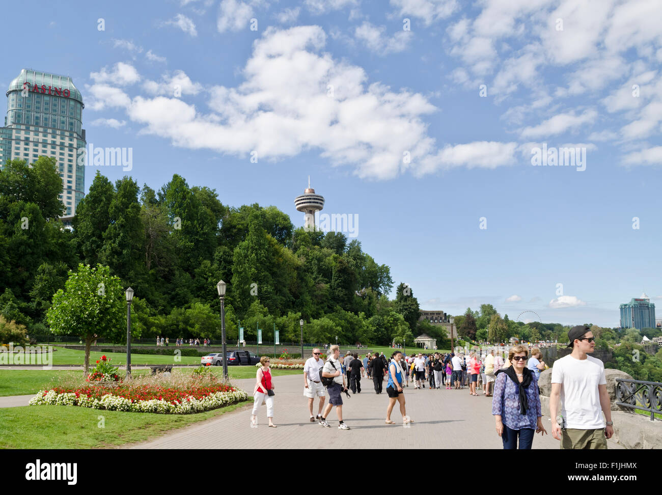 Tourists walking along the promenade by Niagara Falls on the Canadian side.  Fallsview Casino and Skylon tower in the distance. Stock Photo