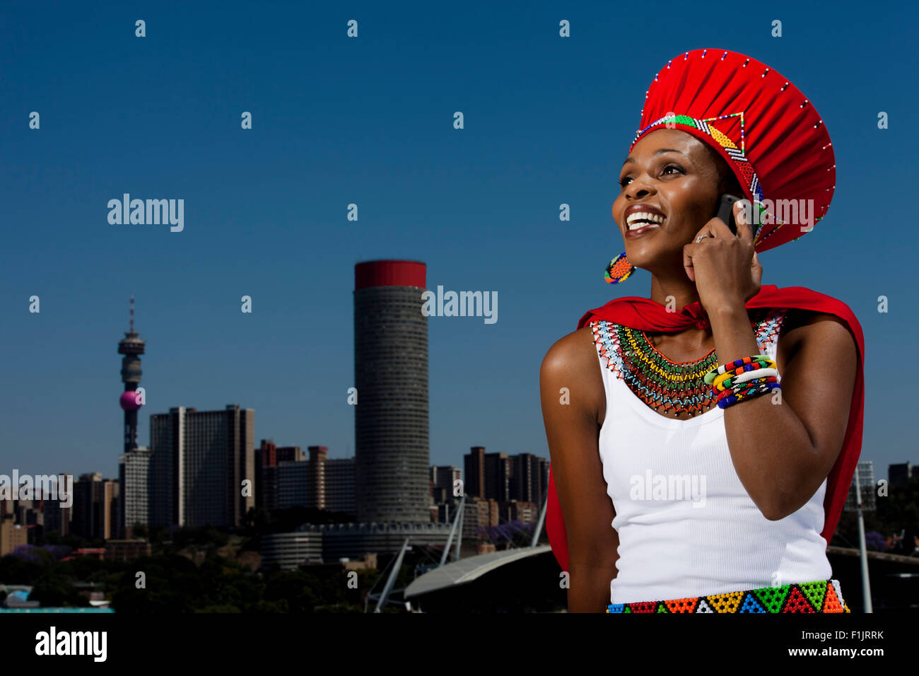 Traditionally dressed African woman talks on cellphone with cityscape in background Stock Photo