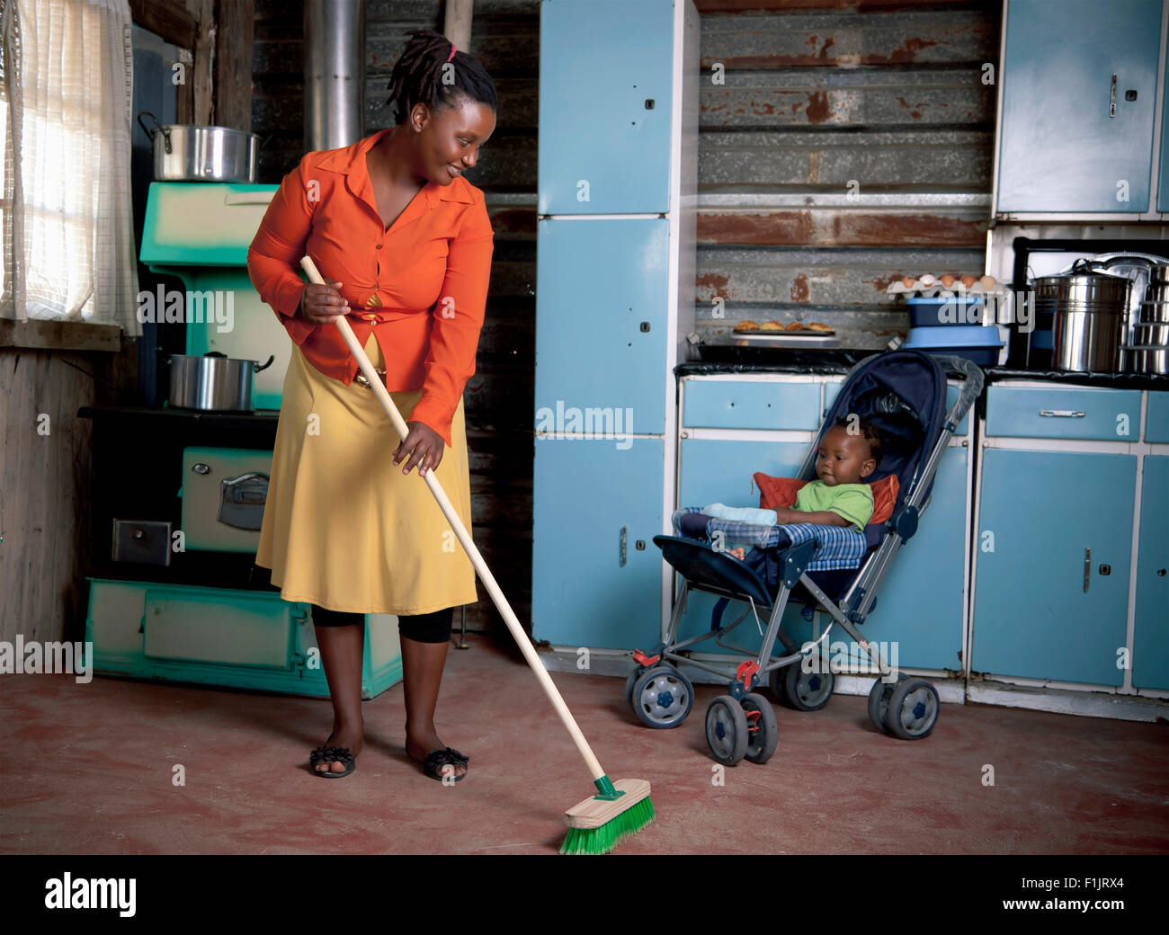 https://c8.alamy.com/comp/F1JRX4/young-black-mother-sweeping-the-floor-inside-her-rural-home-with-her-F1JRX4.jpg