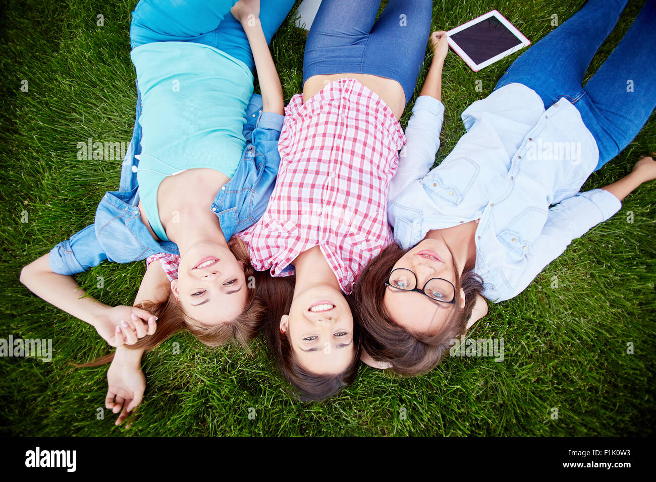 Modern teen girls in casualwear lying on green grass Stock Photo