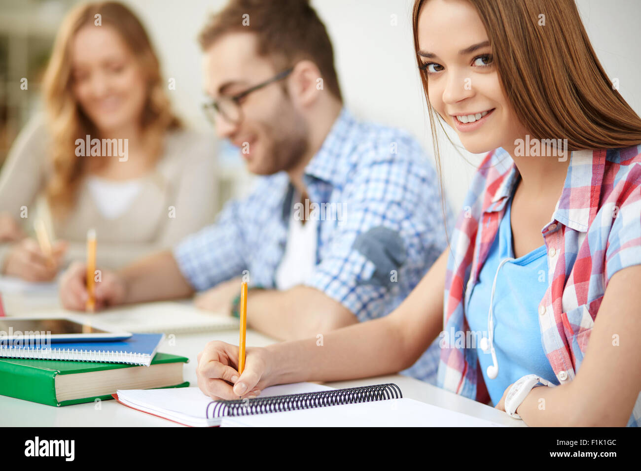 Smiling girl carrying out written task with her groupmates on background Stock Photo