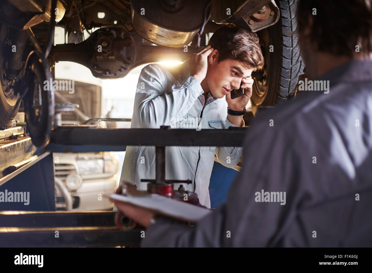 Mechanic and customer talking on cell phone under car Stock Photo
