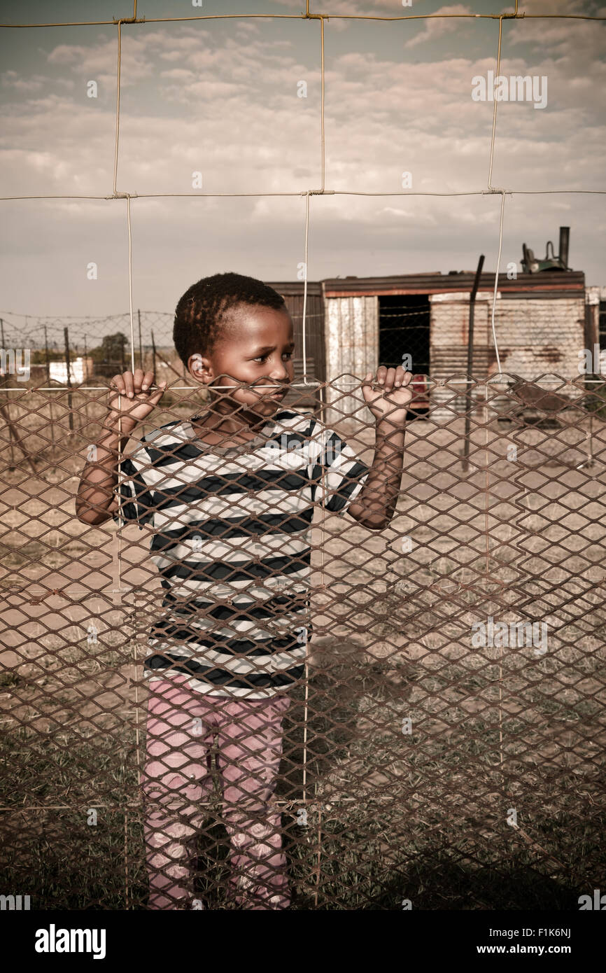 Young African boy stands at a fence Stock Photo