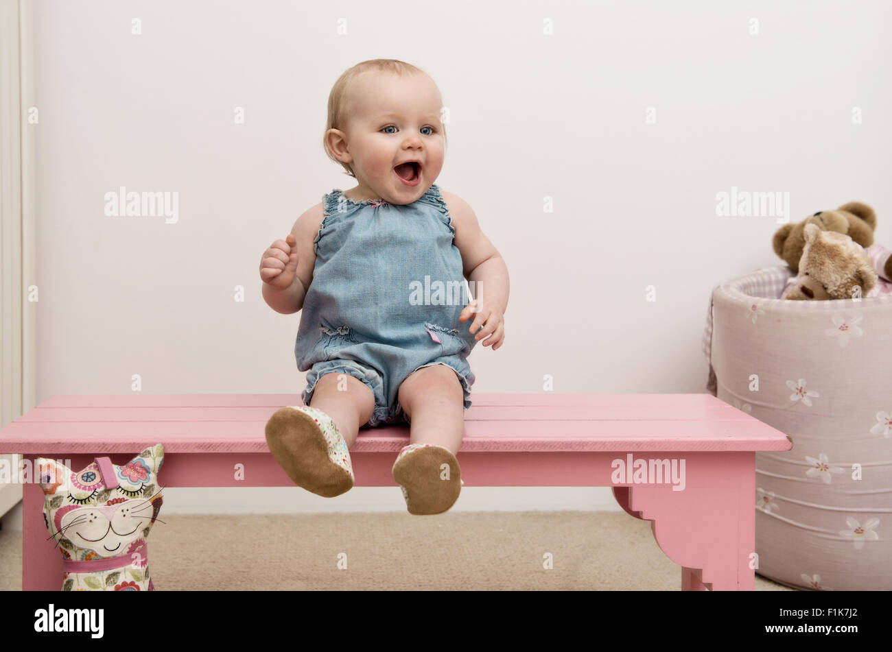 Laughing infant sitting on a pink bench, looking at camera Stock Photo