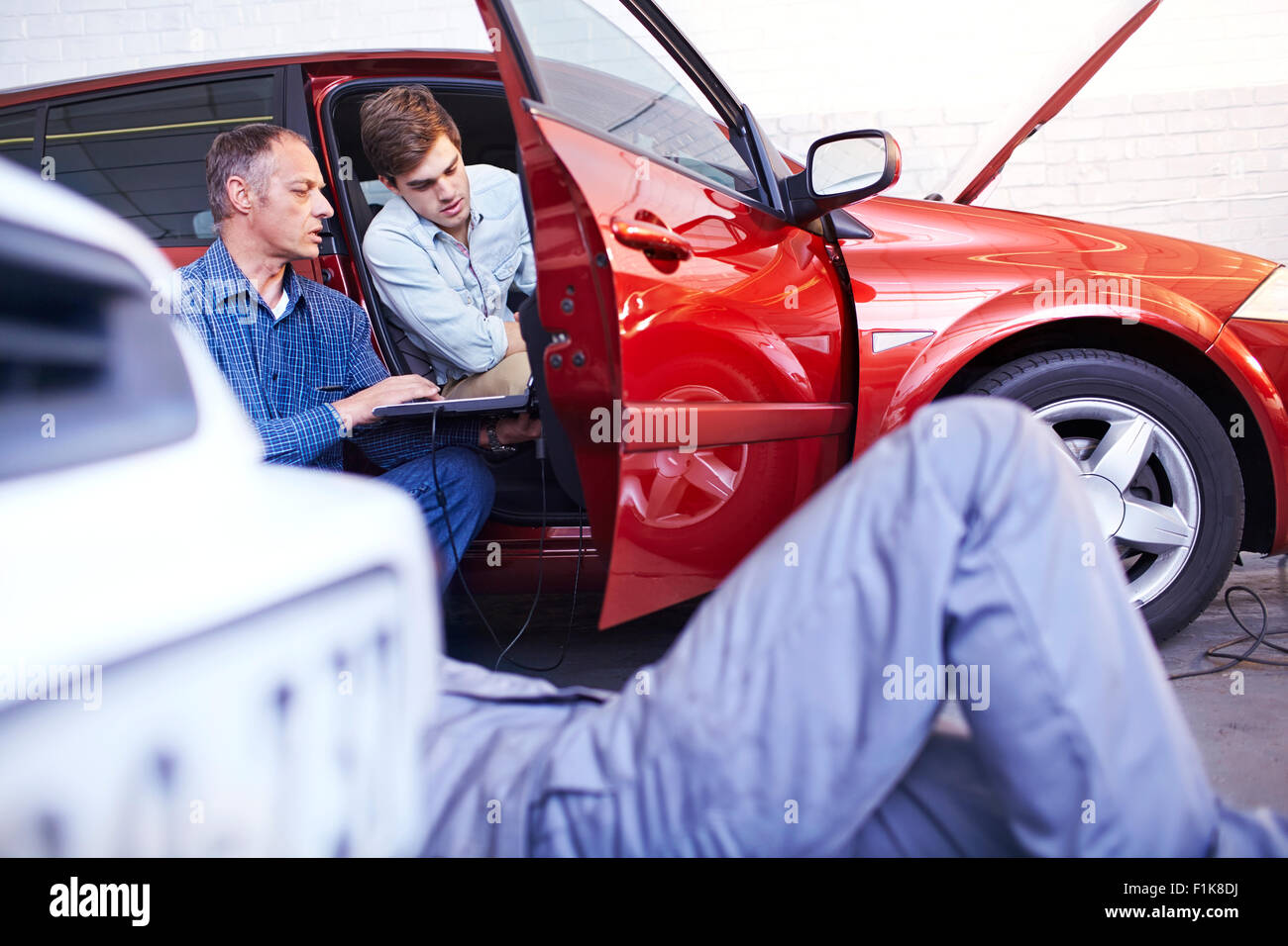 Mechanics with laptop talking at car in auto repair shop Stock Photo