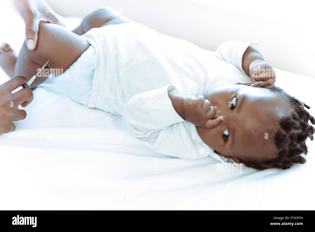 African infant lying on a ward bed being injected by doctor Stock Photo