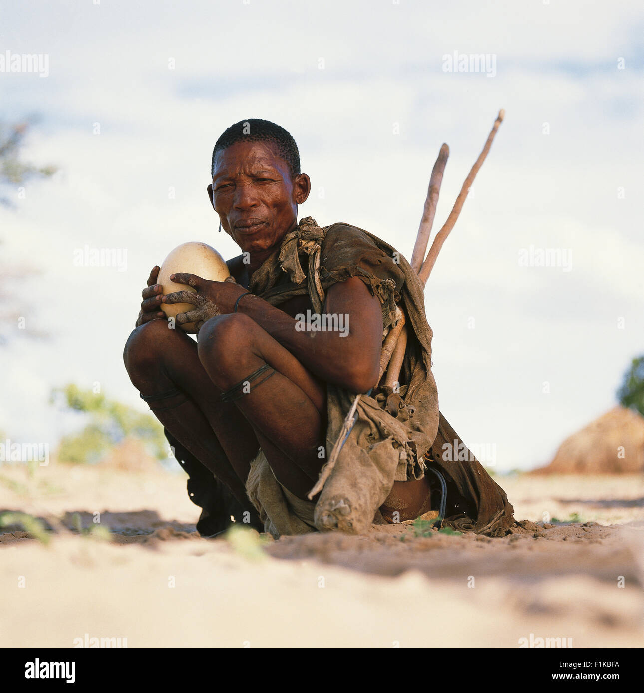 Bushman crouching outdoors holding ostrich egg. Botswana, Africa Stock Photo