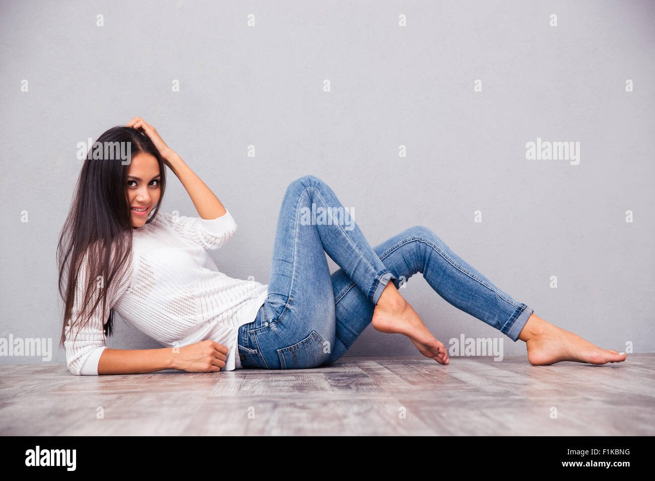 Portrait of a smiling attractive woman lying on the floor on gray background Stock Photo