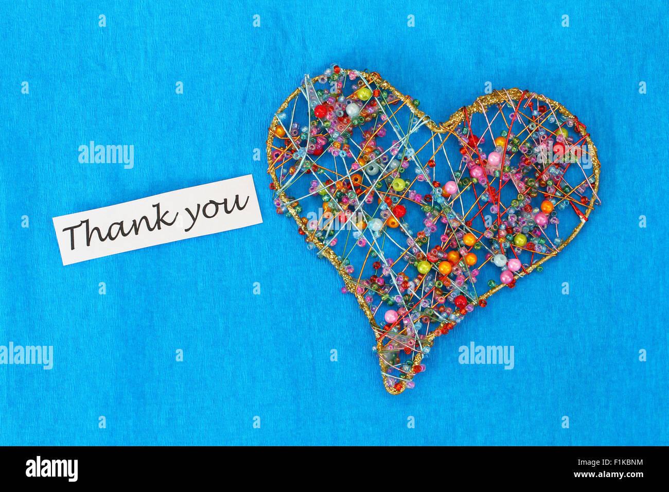 Thank you card with heart made of beads on blue background Stock Photo