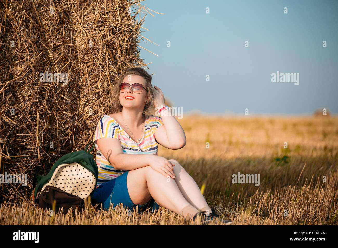 Beautiful Plus Size Young Woman In Shirt Posing In Summer Field Meadow On Hay Bales At Sunset Background Stock Photo