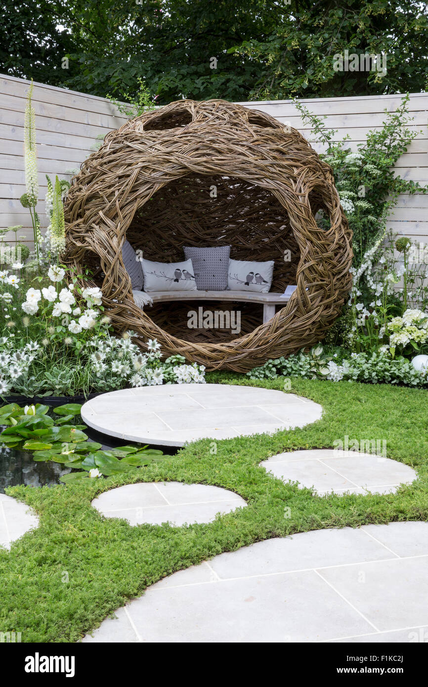 A small urban wildlife bird friendly garden chamomile lawn stepping stones and a woven willow pod with bench and cushions - white flowers Summer UK Stock Photo