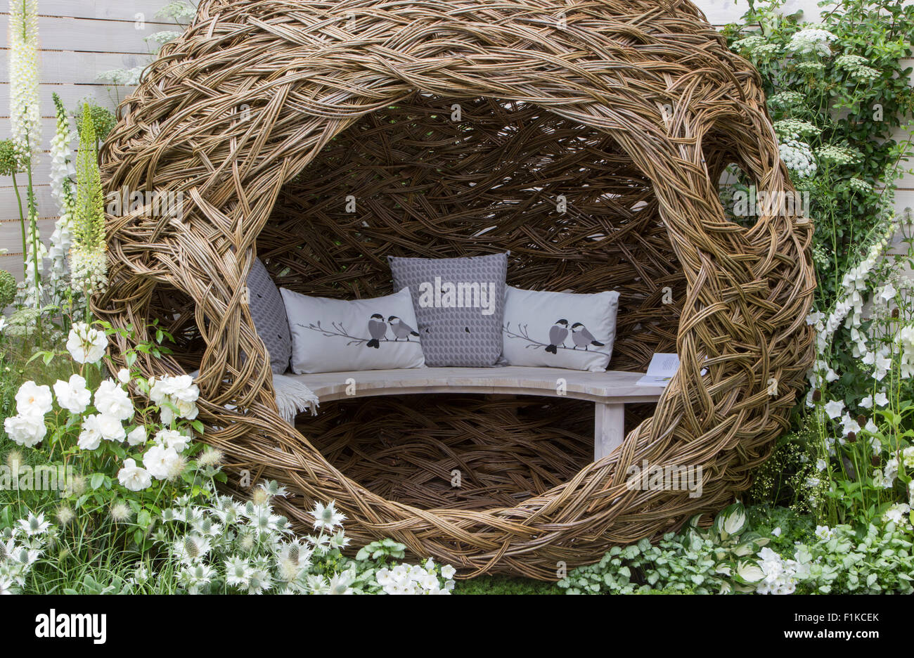 Garden with Modern patio woven willow structure bench bird cushions border planted with white flowering flowers plants painted white fence UK Stock Photo