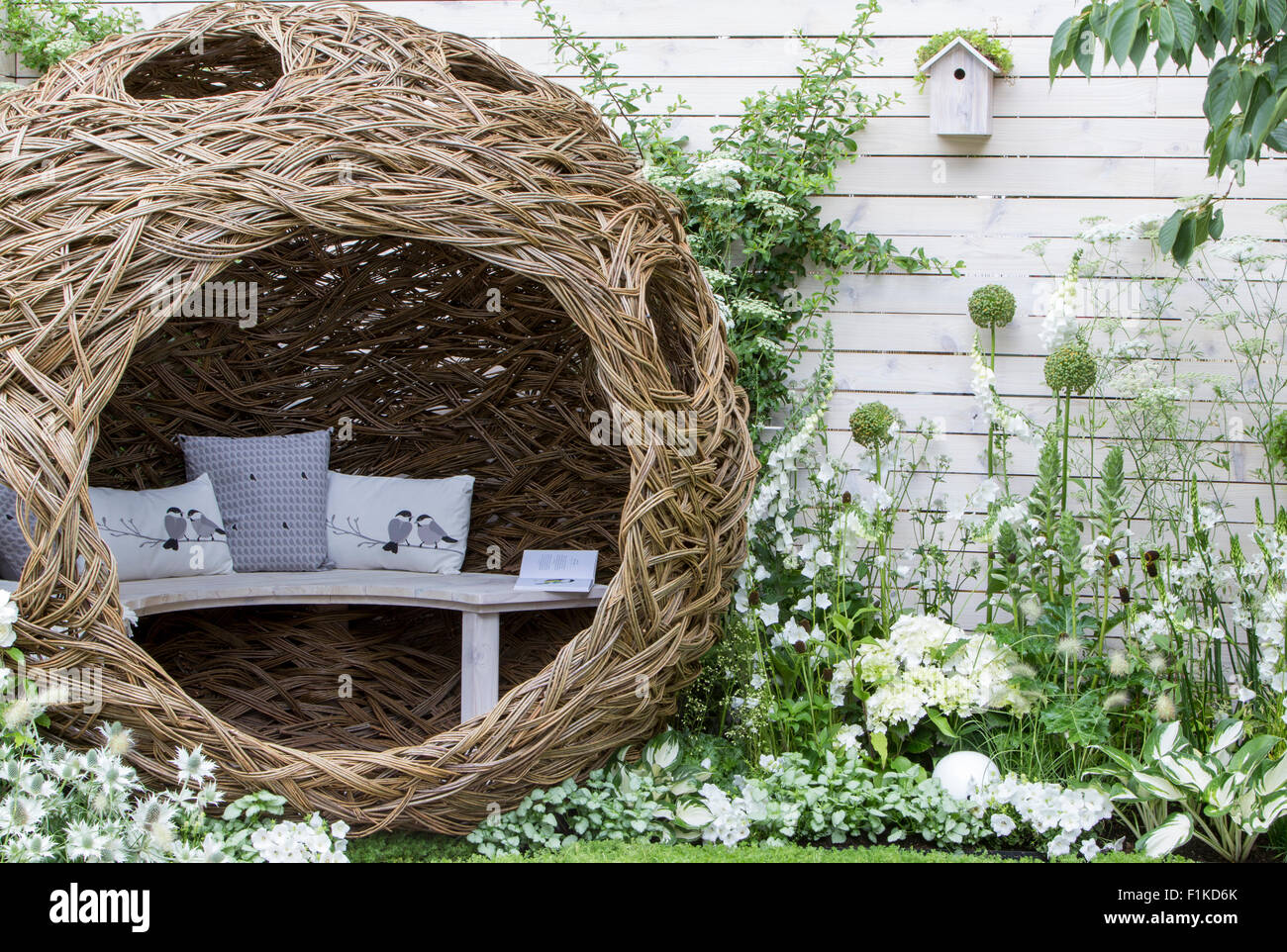 Garden with Modern patio woven willow structure bench bird cushions border planted with white flowering flowers plants painted white fence bird box UK Stock Photo