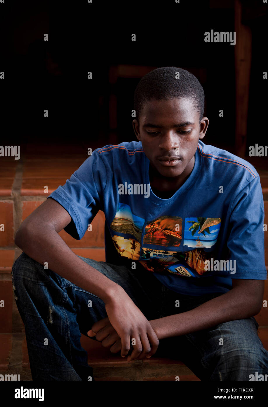 An African teenage boy sitting outside, looking somber Stock Photo - Alamy