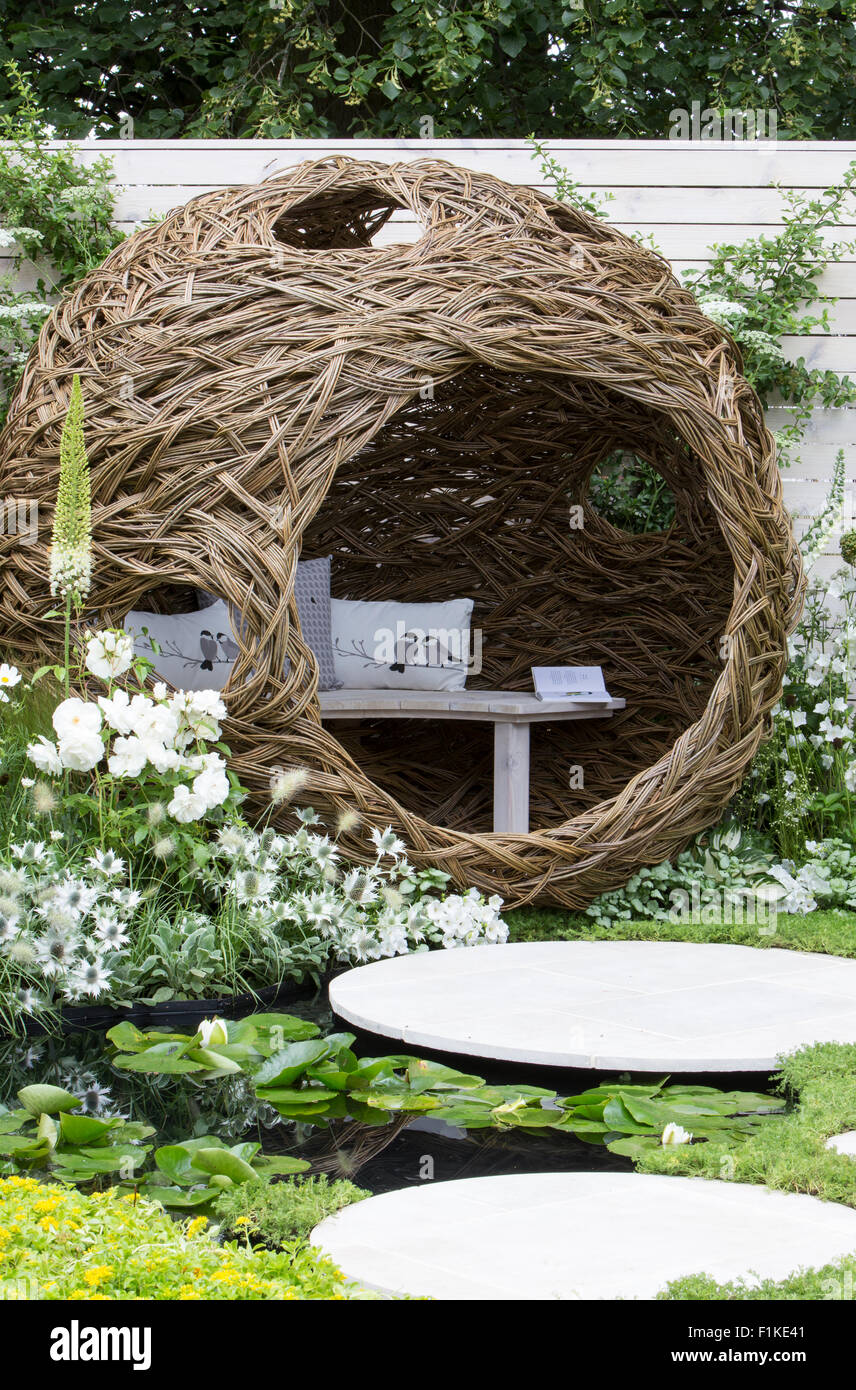 Circular English Garden with Modern patio woven willow structure bench border planted with white flowering flowers plants painted white fence UK Stock Photo