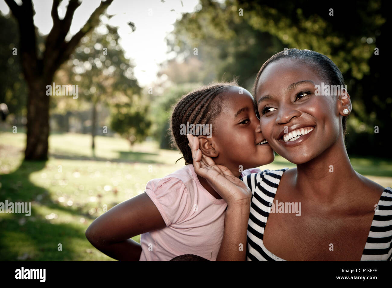 Young African girl kissing her mother on the cheek in a park Stock Photo