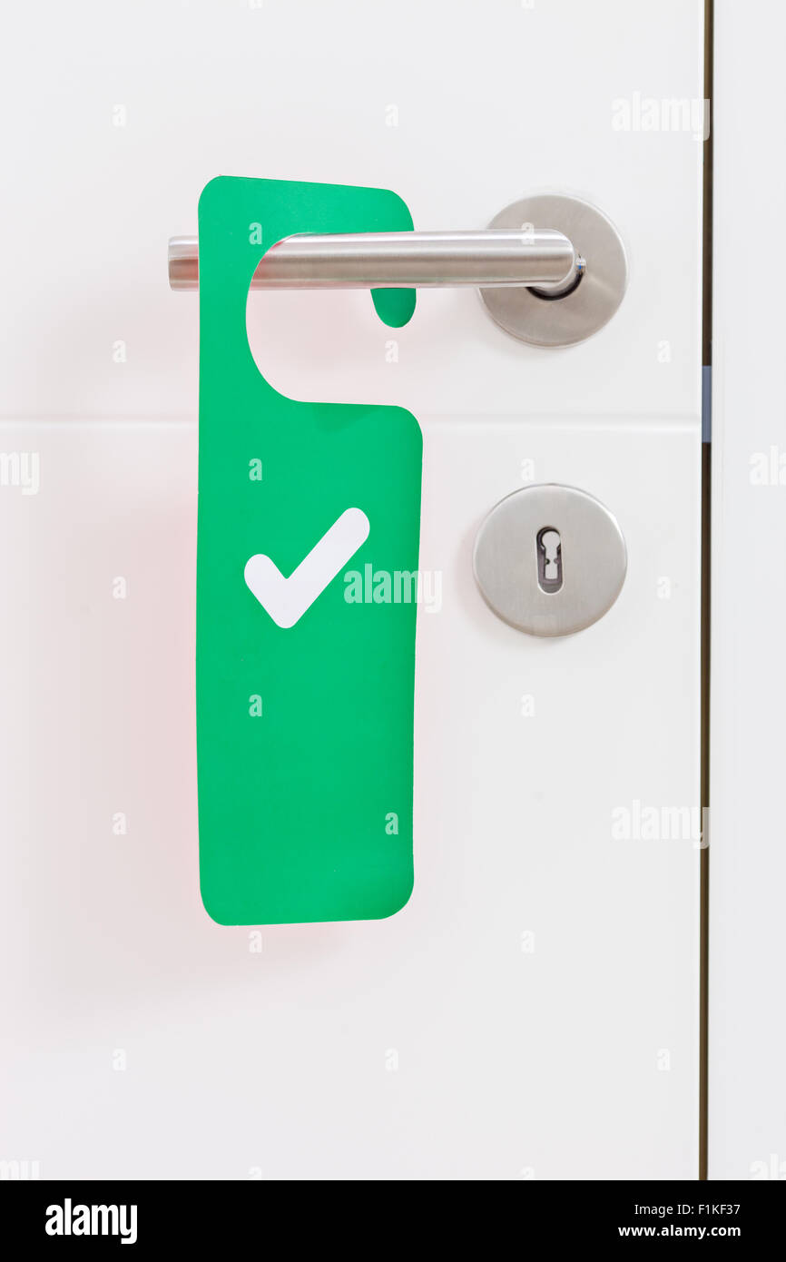 Close-up on a metal handle of a white door with a green access plate with check mark on it Stock Photo